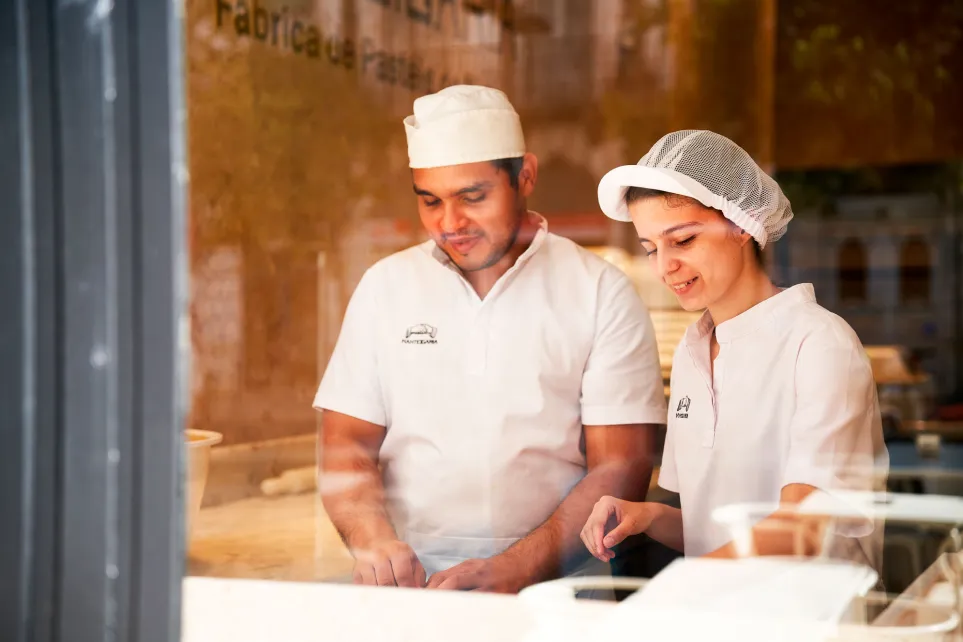Dois padeiros da Manteigaria a trabalhar na fábrica, vistos através da montra da loja