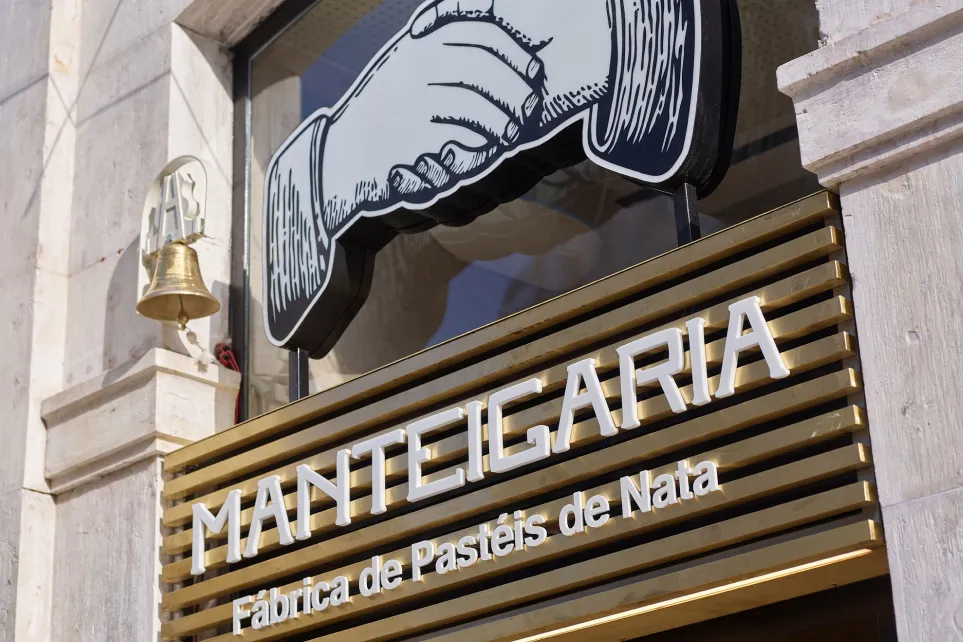 Fachada de uma loja Manteigaria, com o logótipo das mãos e o letreiro Fábrica de Pastéis de Nata