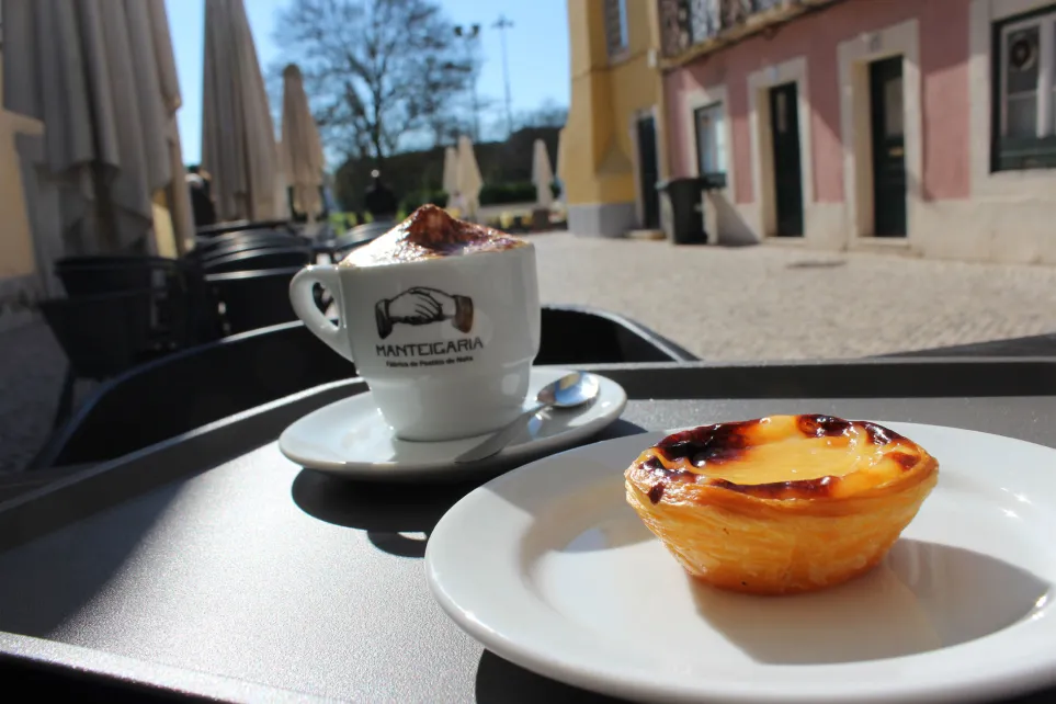 Café y pastel de nata en una taza y plato Manteigaria, en una terraza al aire libre