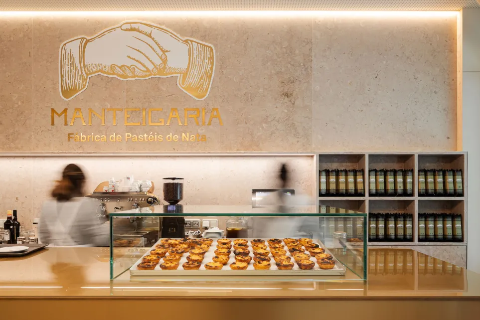 Balcão da docesecafe.live tabuleiro de pastéis de nata sob o logótipo dourado das mãos