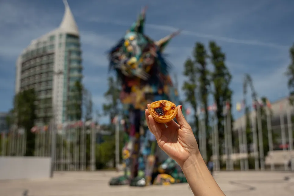 Mão a segurar um pastel de nata em frente à escultura do Lince Ibérico, no Parque das Nações