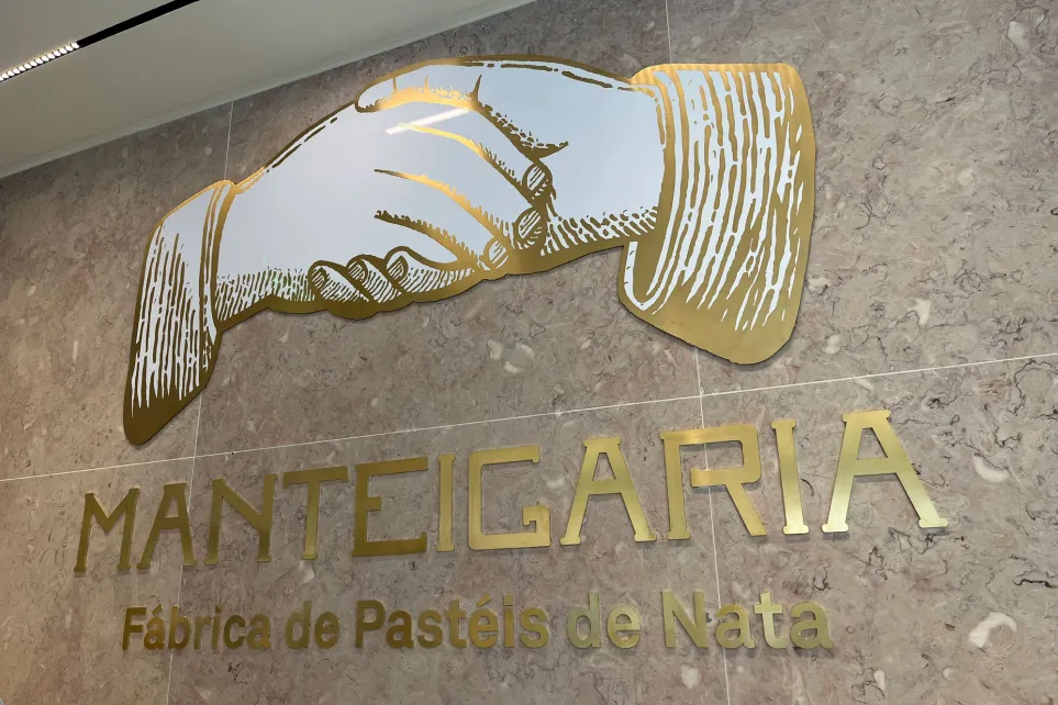 Logótipo das mãos da Manteigaria em dourado, sobre parede de mármore