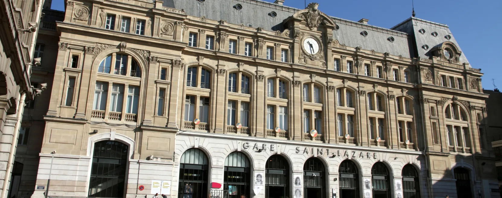 Fachada da estação Gare Saint-Lazare em Paris, com relógio e o nome gravado na pedra