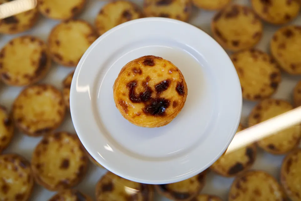 Pastel de nata visto de cima, num prato branco, rodeado de outros pastéis desfocados