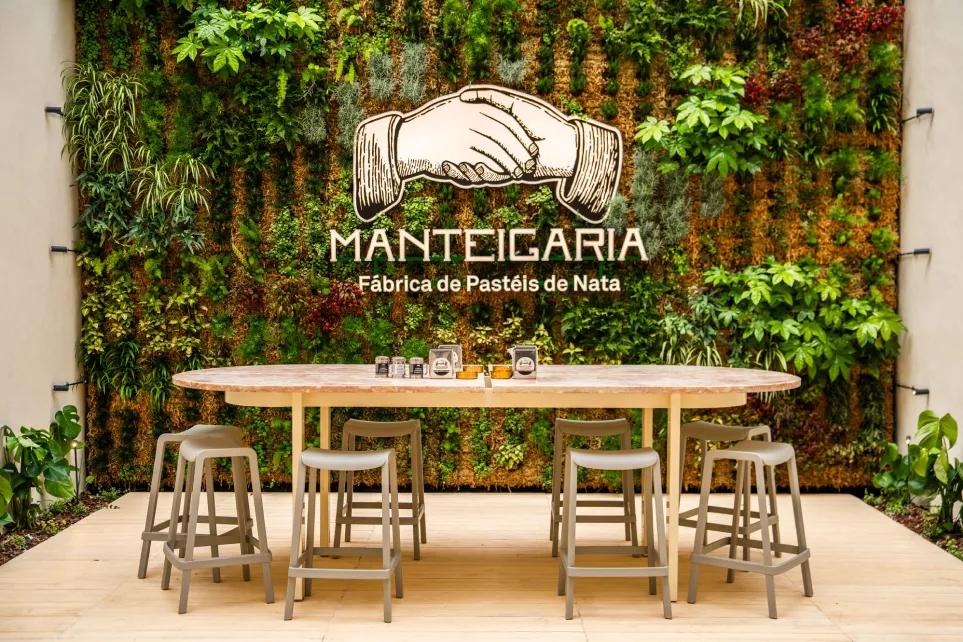 Vertical garden wall with the golden Manteigaria logo and a communal table