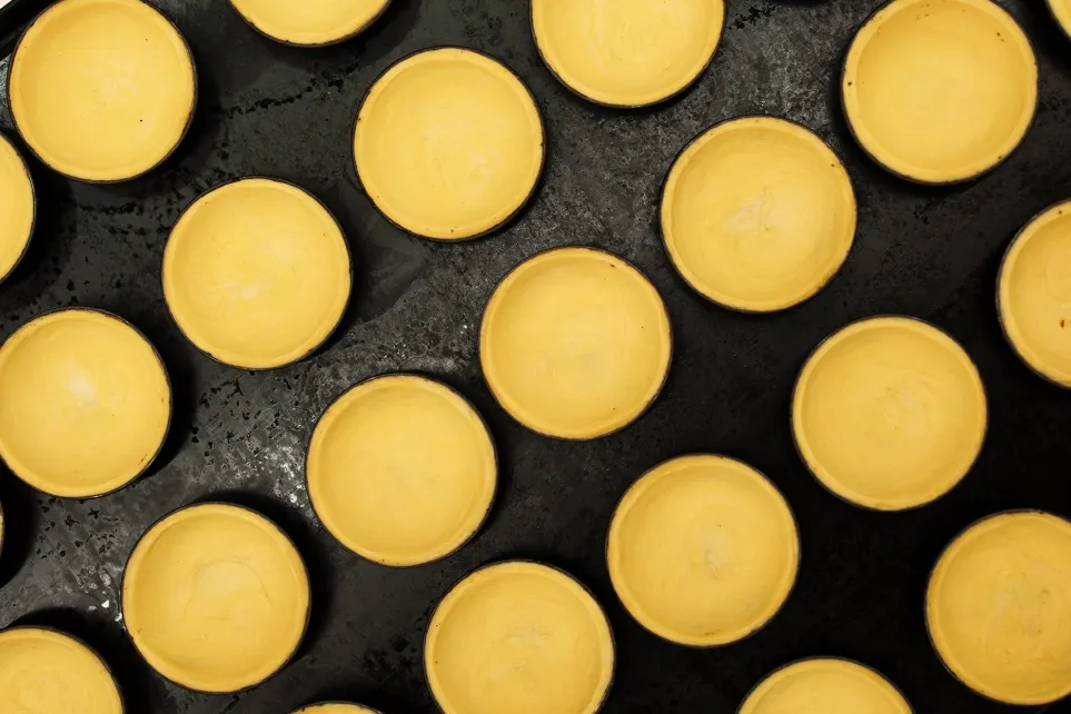Massa de pastel de nata moldada dentro de formas metálicas, vista de cima, antes de ir ao forno