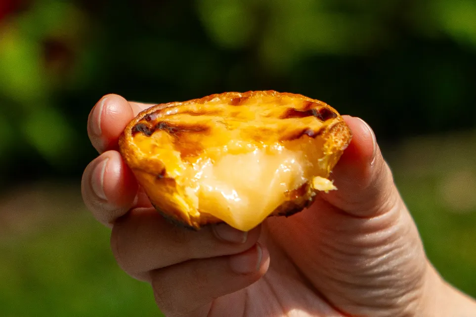 Pastel de nata tout juste sorti du four, tenu à la main avec la crème qui déborde