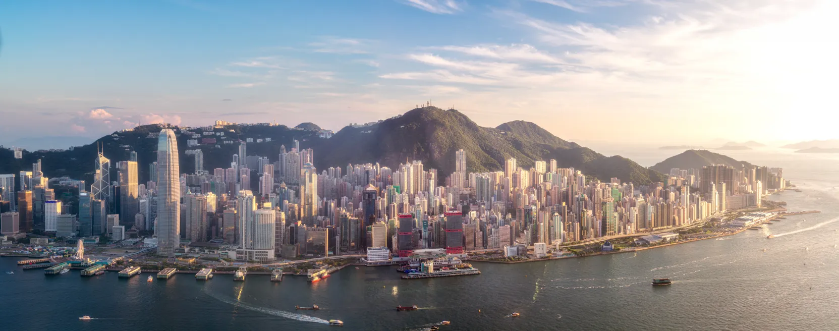 Vista aérea da baía de Hong Kong ao entardecer, com arranha-céus e barcos