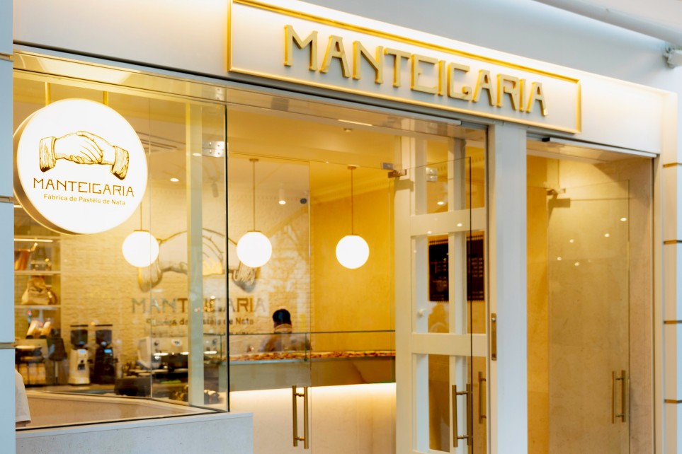 Fachada dourada da docesecafe.live o logótipo iluminado e montras com produtos