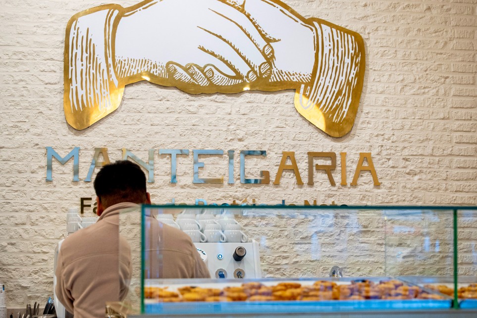 Homem a preparar café atrás do balcão da Manteigaria, com o logótipo das mãos na parede