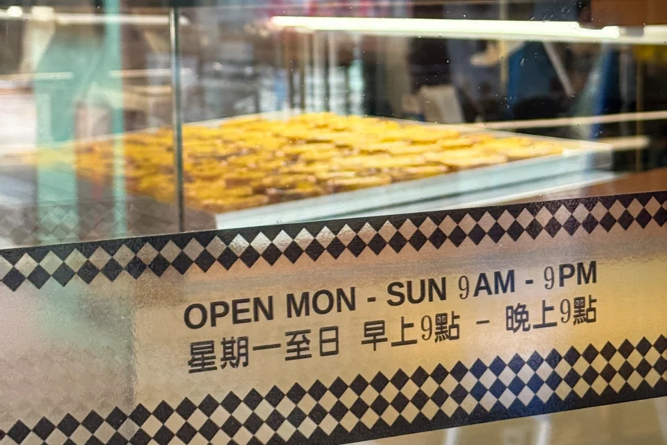 Plateau de pastéis de nata en vitrine, avec les horaires d'ouverture en anglais et en chinois