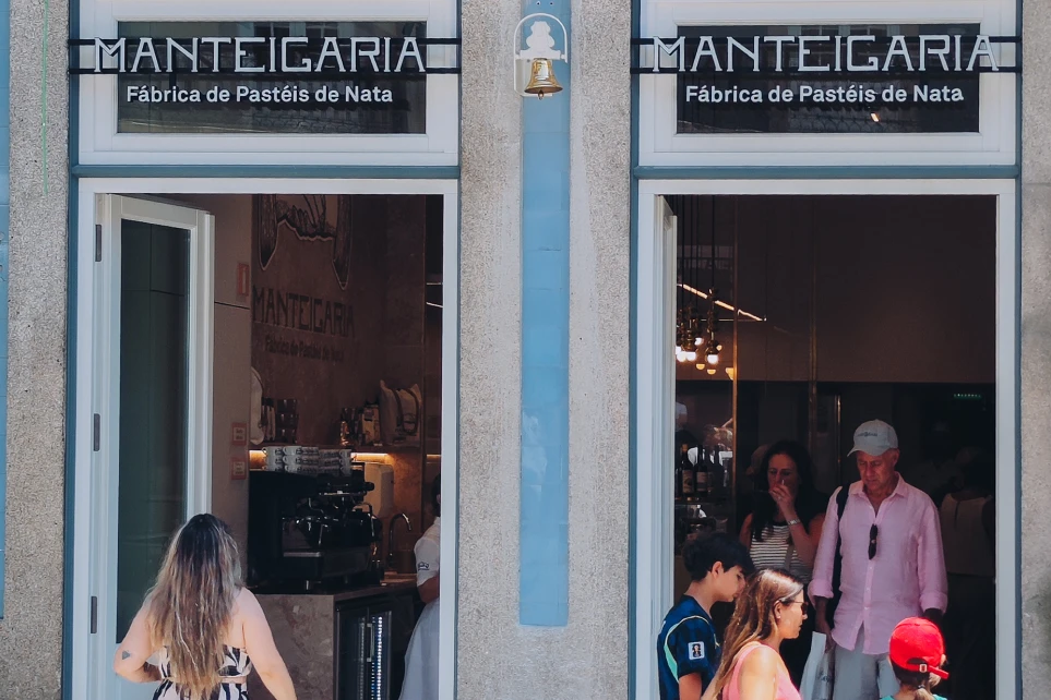 Manteigaria façade with two Pastel de Nata Factory signs and a bell in the centre