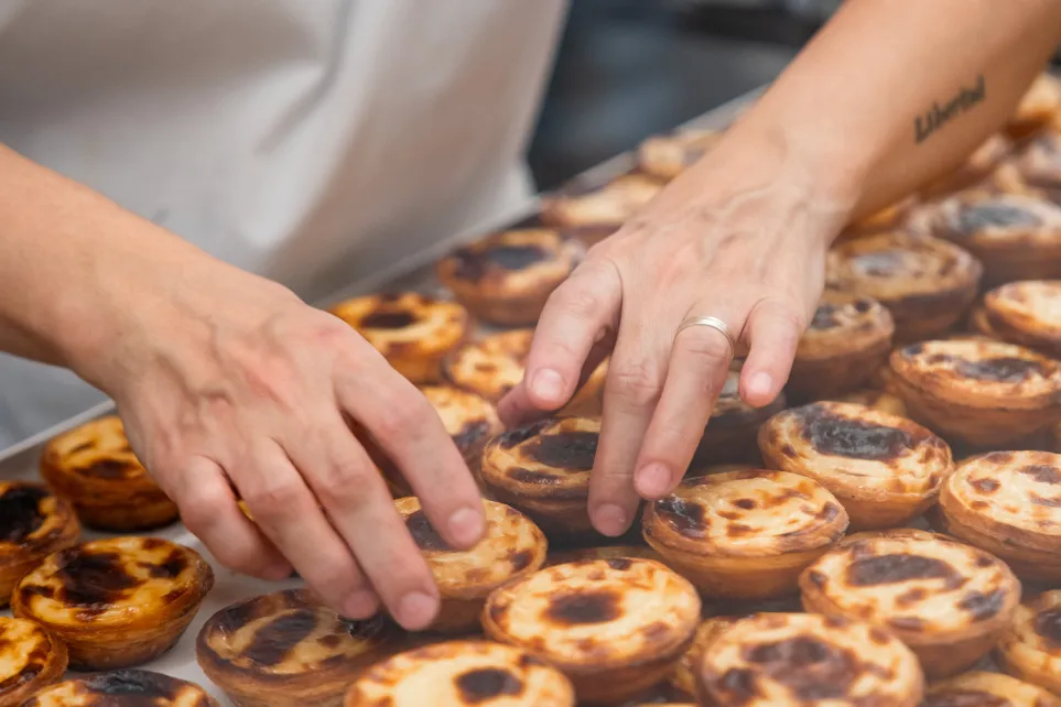 Manos colocando pasteles de nata en una bandeja